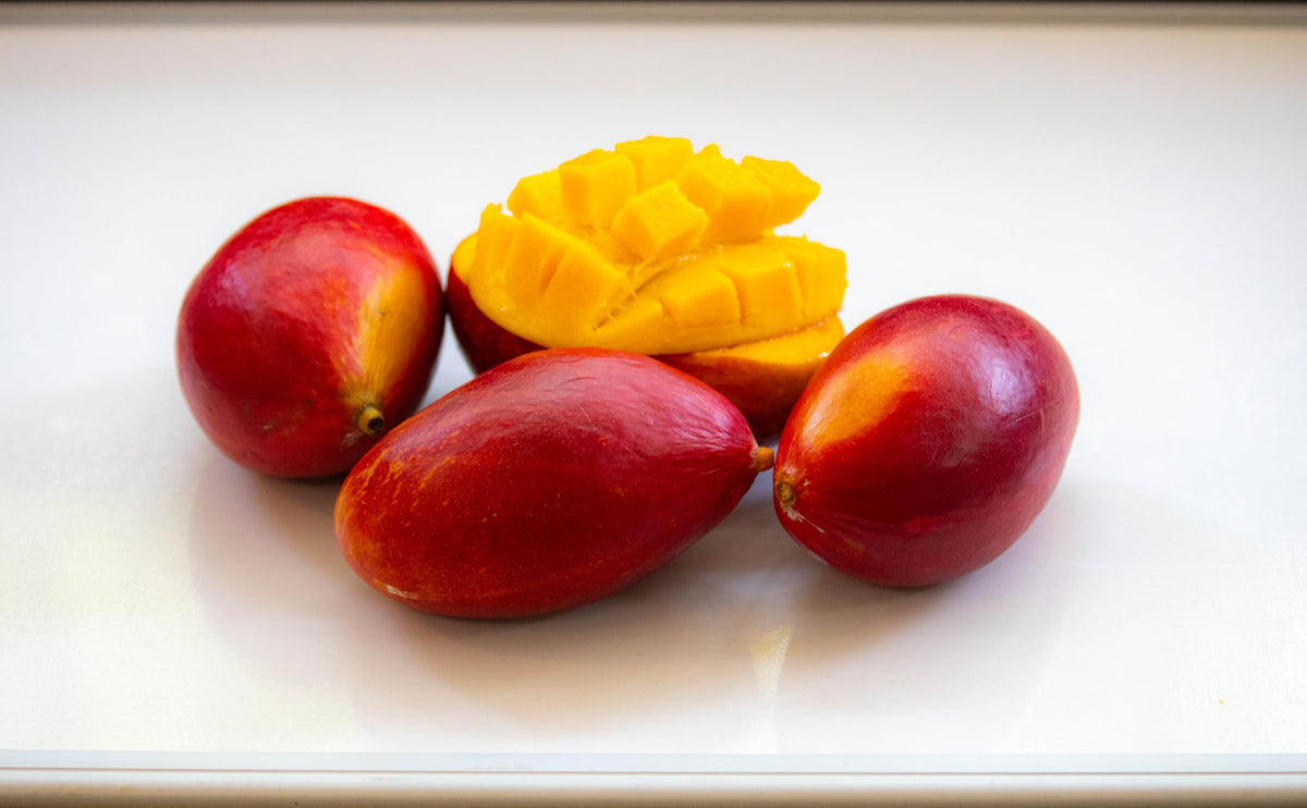 Whole red mango fruits and a cut mango.